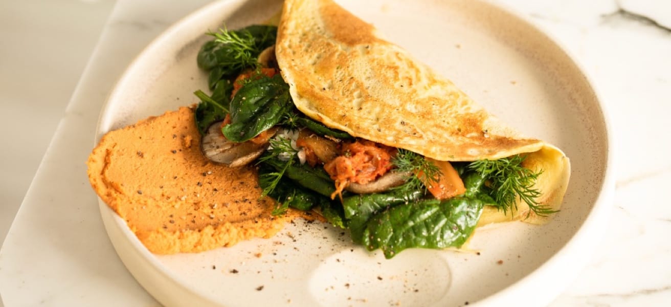 A folded omelette on a plate, served with mushrooms and herbs